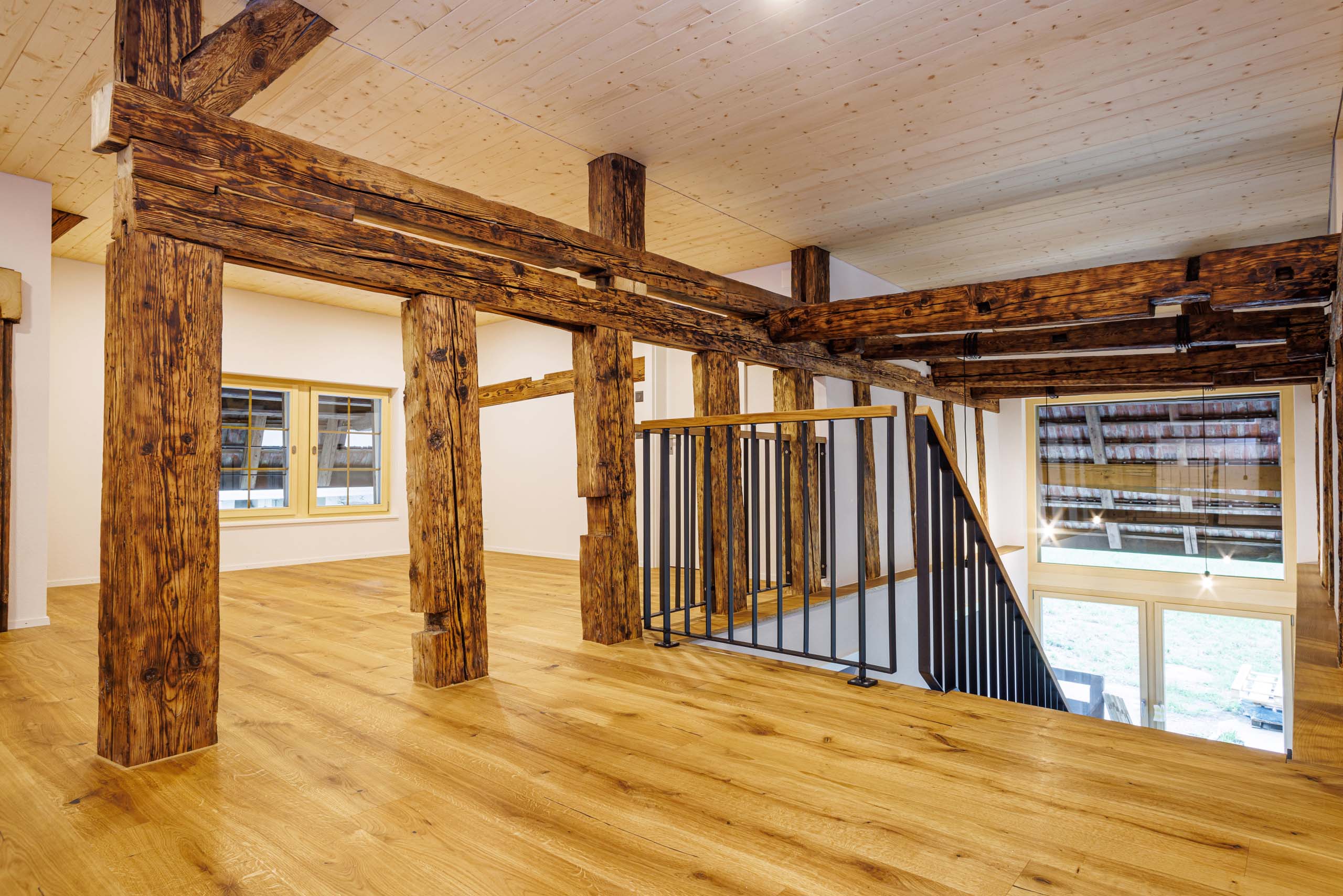 Ein heller Raum mit Naturholzparkett, originalen Holzpfeilern des umgebauten Bauernhaueses und einer hellen Holzdiele mit weiss gestrichenen Wänden - geplant und umgesetzt von der Kobi Architektur AG in der Region Bucheggberg