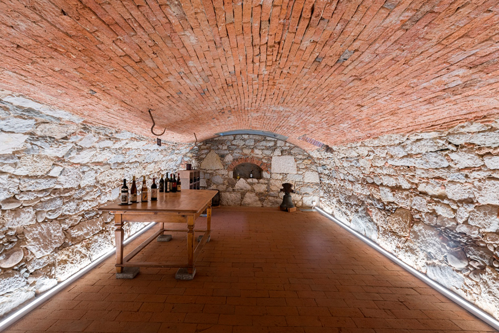 Renovierter Gewölbekeller eines umgebauten Bauernhauses im Buechibärg mit einem neuen Ziegelplattenboden, originalen Steinwänden, einer gewölbten Ziegeldecke und beleuchteten Sockelleisten - geplant und realisiert von der Kobi Architektur AG in Biezwil (Solothurn)