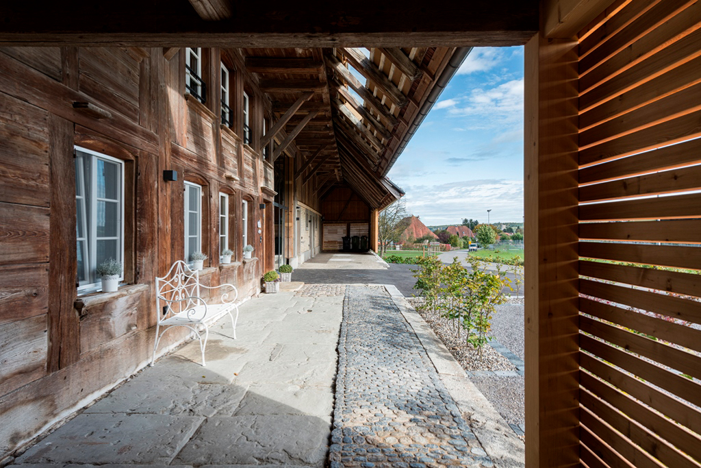 Umgebautes rustikales Bauernhaus von Aussen mit einer weissen Sitzbank, einem Vorplatz aus Steinboden und einigen kleinen Grünpflanzen. Umgebaut von der Kobi Architektur AG in Biezwil im Buechibärg